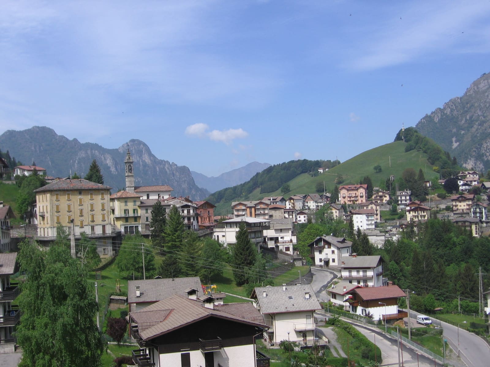 Le case e il campanile di Oltre il Colle sui prati, con le cime rocciose della conca sullo sfondo